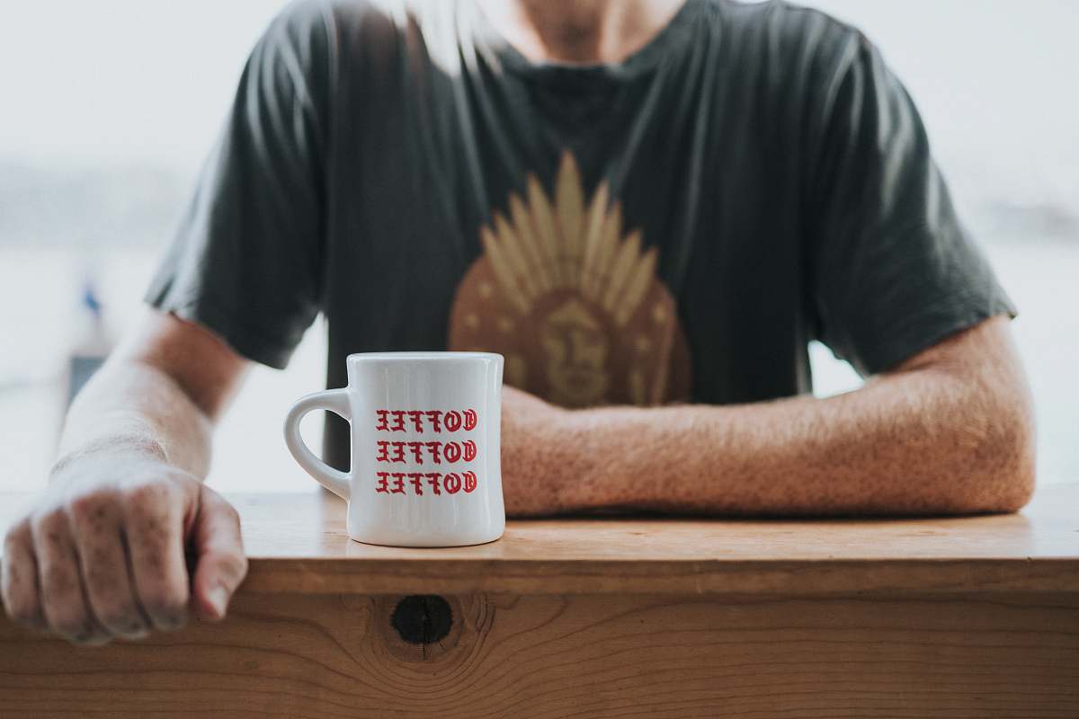 coffee cup man in green and brown t-shirt sitting by the bar table with white coffee mug manhattan beach pier